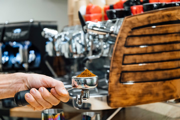 Detail of man hand holding portafilter recipient filled with coffee ground while preparing espresso