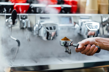 Detail of man hand holding portafilter recipient filled with coffee ground while preparing espresso