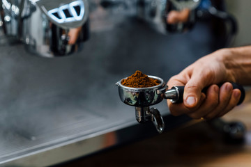 Detail of man hand holding portafilter recipient filled with coffee ground while preparing espresso