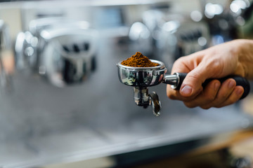 Detail of man hand holding portafilter recipient filled with coffee ground while preparing espresso