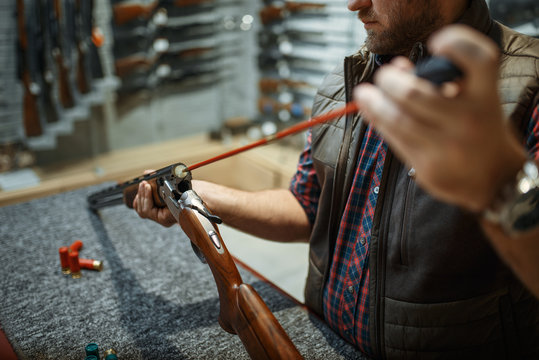 Man cleans rifle barrel at counter in gun shop