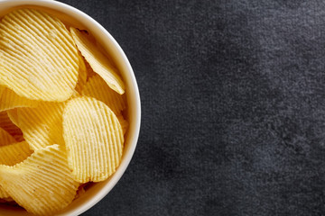 Crispy potato chips in a white bowl on black background