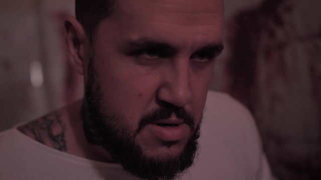 Crazy man in straitjacket tied to a chair, killer psychopath in a room with bloodied walls