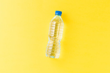 Overhead shot of mineral water in small plastic bottle on yellow background with copyspace