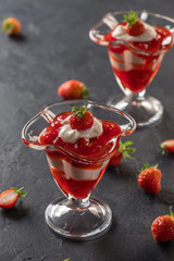 Cream dessert with fresh strawberries and strawberry jam in a glass bowl on a dark background