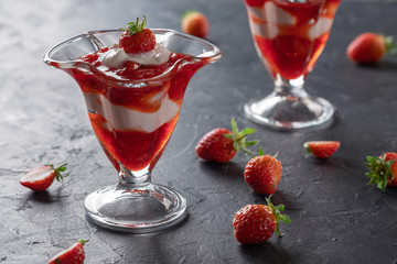 Cream dessert with fresh strawberries and strawberry jam in a glass bowl on a dark background