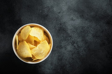 Crispy potato chips in a white bowl on black background