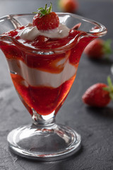 Cream dessert with fresh strawberries and strawberry jam in a glass bowl on a dark background