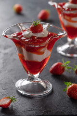 Cream dessert with fresh strawberries and strawberry jam in a glass bowl on a dark background