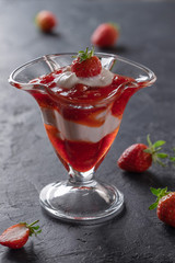 Cream dessert with fresh strawberries and strawberry jam in a glass bowl on a dark background
