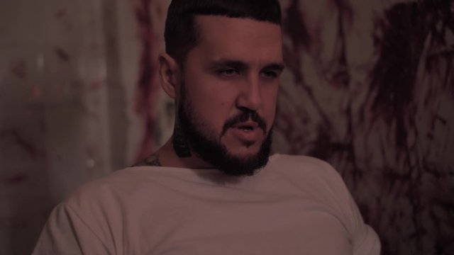 Crazy man in straitjacket tied to a chair, killer psychopath in a room with bloodied walls