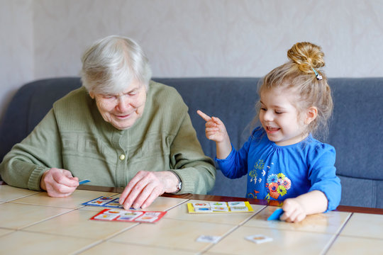 Beautiful toddler girl and grand grandmother playing together pictures lotto table cards game at home. Cute child and senior woman having fun together. Happy family indoors