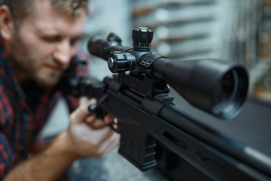 Man checks optical sight on sniper rifle, gun shop