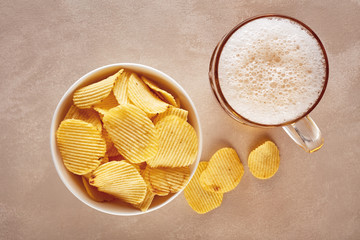 Potato chips and glass of beer on rustic wooden background. Top view