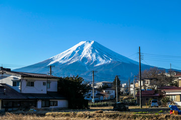 Mt Fuji towering above the Fujiyoshida city, seen from the city level. The mountain is positioned directly behind the city. Small city at the foothill of holly mountain
