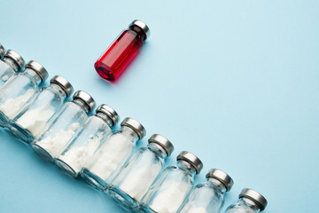 A row of medical vials. Glass bottles with powder for injection and one with red potion on a light background.