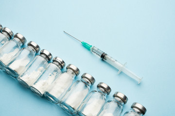 Row of medical vials and syringe. Glass bottles with powder for injection on a light background.