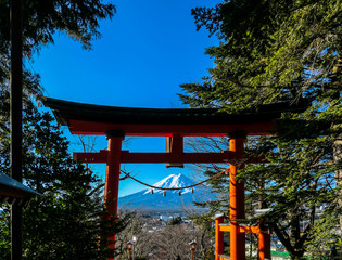 Distant view on Mt Fuji, framed in between orange Torri gate, leading to Chureito Pagoda in Japan, on a clear, wintery day.The top parts of the volcano are covered with a layer of snow. Holly mountain