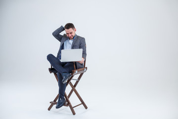 Male teacher director businessman sitting on a chair studying documents. He is looking at the laptop screen. New business project.