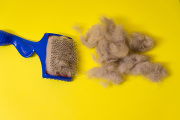 Comb for animal hair and gray wool on a yellow background. Animal hairbrush.