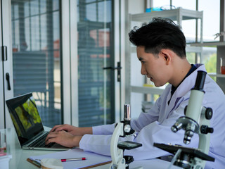 Th Young medical doctor scientist was doing research study with microscope and notebook computer in clinical laboratory for Virus infection prevention and cure