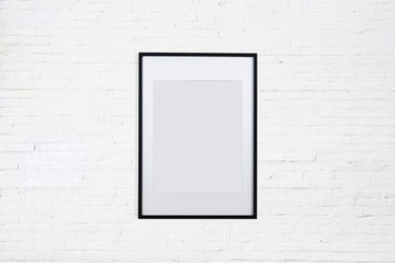 Black photo frame on a white brick wall. Template or mockup for text or design