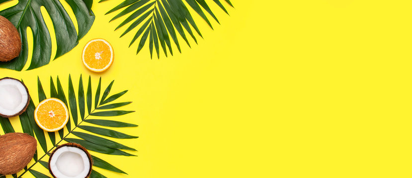 Summer tropical composition. Frame of Green tropical leaves of palm trees and monstera, coconut, orange on bright yellow background. Flat lay, top view, copy space. Creative background food, fruit