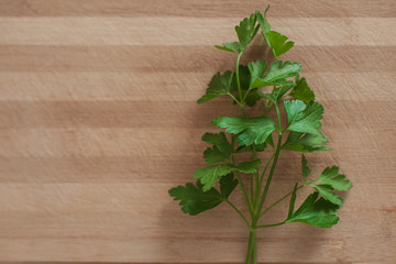 Close up of parsley leaves, from the right side of the frame, on top of a wooden surface. Landscape format