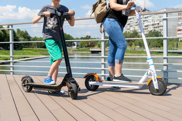 A young boy and a woman ride two electric scooters in a park. Sunny summer day. Modern city transport. City park near the river.