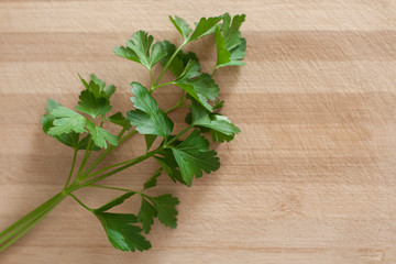 Close up of parsley leaves, from the left side of the frame, on top of a wooden surface. Landscape format