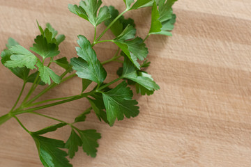 Close up of parsley leaves, from the left side of the frame, on top of a wooden surface. Landscape format