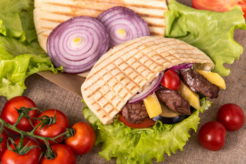 Pita doner kebab with green salad, potato free, tomatoes, cherry, cucumber and fried beef. Street food. Fast food. Doner kebab