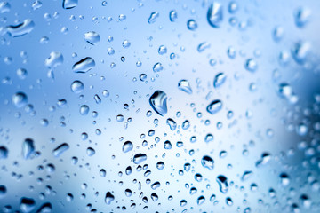 Wet glass with raindrops closeup on blue sky background_