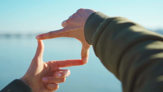POV first person view female hands making frame with fingers on blue sky bay and cityscape background