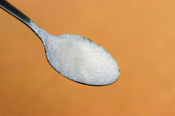 Teaspoon with white sugar on orange background. Sugar for coffee_
