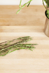 A bunch of wild asparagus lies on a wooden top with a close up of some points coming from the top, in a home kitchen.