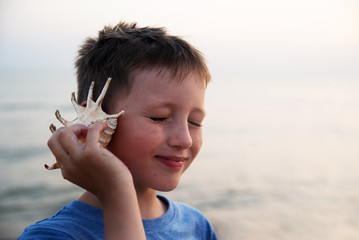 A blind boy listens to the sound of the sea, leaning a seashell against his ear.