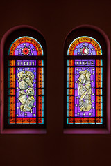 Stained glass window in old christian church. Colorful spectrum glass. Interior of cathedral with artwork element. Ancient craftsmanship inside of building. Purple, red, yellow tint on religion art.