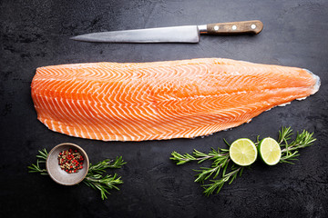 Fresh raw salmon or trout sea fish fillet with spices and herbs on black background, top view