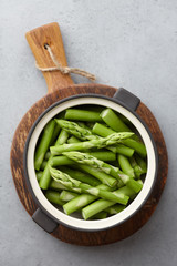 Fresh green asparagus in bowl on gray background