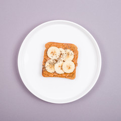 One sandwich with peanut pasa and banana on a white plate on a gray table. Healthy breakfast concept.