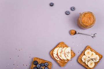 Fototapeta na wymiar Sandwiches with peanut butter and fruits and seeds on a gray background. Healthy vegetarian breakfast. Top view, flat lay, copy space.