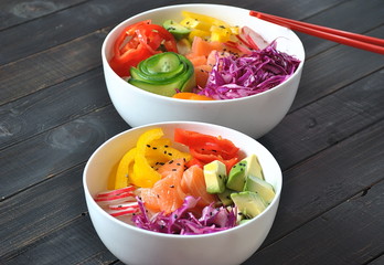 Poke bowls with fresh salmon, crystal noodles, radish, avocado, sweet pepper, cucumber, sesame seeds, red cabbage. Organic food. Fresh seafood recipe. Food concept poke bowl on wooden background