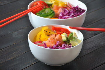 Poke bowls with fresh salmon, crystal noodles, radish, avocado, sweet pepper, cucumber, sesame seeds, red cabbage. Organic food. Fresh seafood recipe. Food concept poke bowl on wooden background