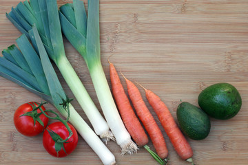 High angle view of some fresh organic veggies on a bamboo board including leeks, carrots, tomatoes, and avocados