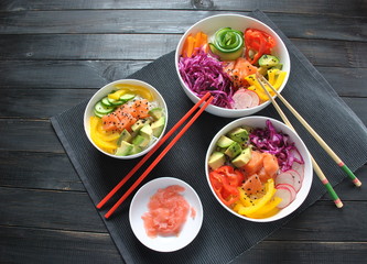 Poke bowls with fresh salmon, crystal noodles, radish, avocado, sweet pepper, cucumber, sesame seeds, red cabbage. Organic food. Fresh seafood recipe. Food concept poke bowl on wooden background