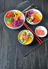 Poke bowls with fresh salmon, crystal noodles, radish, avocado, sweet pepper, cucumber, sesame seeds, red cabbage. Organic food. Fresh seafood recipe. Food concept poke bowl on wooden background