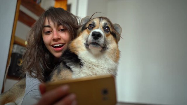 joyful smiling attractive young woman hugging cute corgi dog and taking selfie with pet using phone