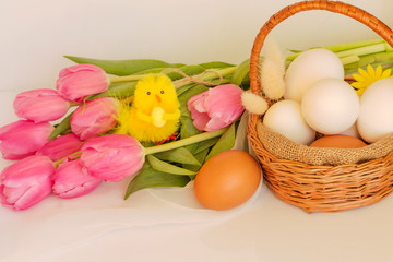 aster composition. Wicker basket with eggs and a bouquet of delicate pink tulips.
