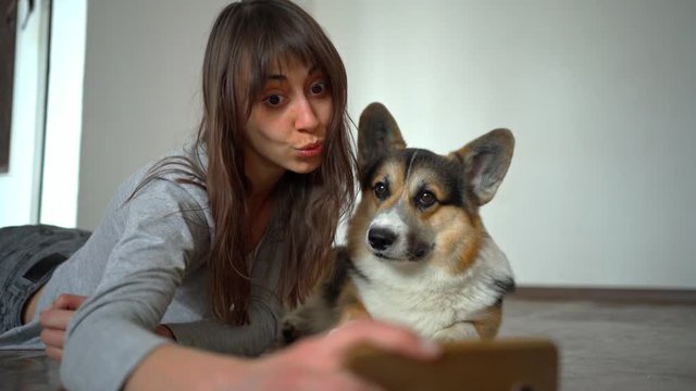 beautiful young girl hugging and kissing her cute curious corgi dog and taking selfie using phone